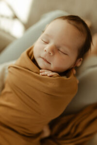 Newborn Photos, A baby sleeps in her dad's lap as sunlight shines in on her face.